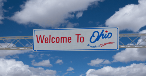 Sign welcoming visitors to Ohio, featuring the text "Welcome To Ohio" against a blue sky with clouds.