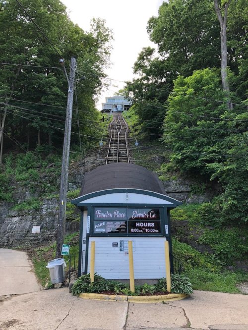 A funicular railway station at the base of a steep hill, surrounded by lush greenery and trees.