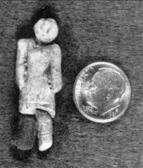 A small carved figure next to a dime for scale, showcasing intricate details on the figure's clothing.