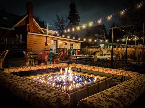A cozy outdoor fire pit surrounded by seating, with string lights illuminating a backyard at night.