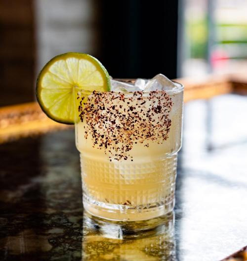 A refreshing cocktail with a lime slice, served in a textured glass, garnished with a rim of chili powder.
