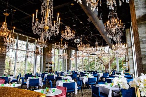 Elegant restaurant interior with chandeliers, blue chairs, and tables set with green drinks, surrounded by large windows.