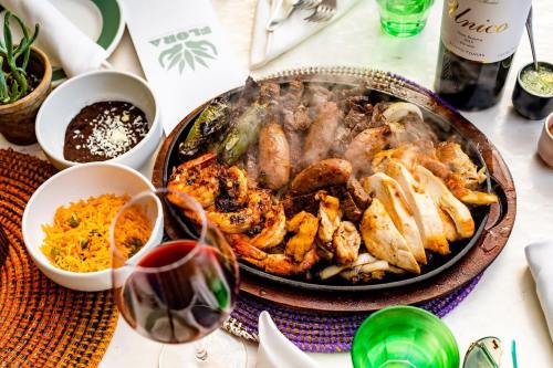 A sizzling platter of grilled meats, including chicken and beef, served with rice, beans, and wine on a colorful table setting.