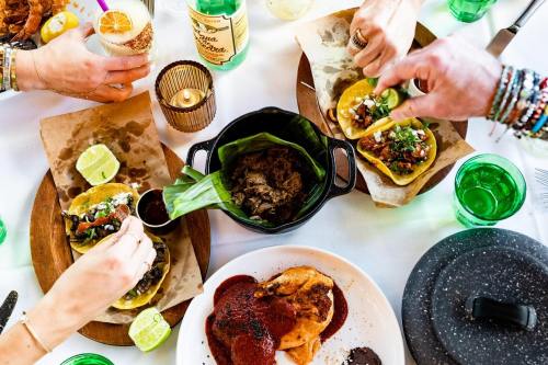 A vibrant table spread with tacos, lime wedges, and drinks, featuring hands preparing and enjoying the meal.