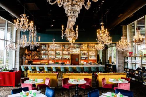 Chic restaurant interior with colorful seating, a bar lined with bottles, and elegant chandeliers hanging from the ceiling.