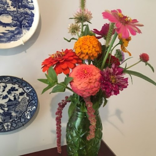 A vibrant bouquet of flowers in a green vase, with decorative plates hanging on the wall behind it.