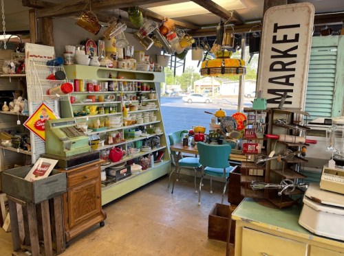 A vintage shop interior featuring colorful kitchenware, shelves of dishes, and retro decor with a market sign.