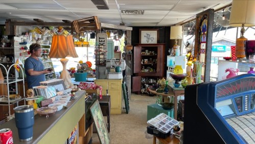 A vintage shop filled with eclectic items, including lamps, decor, and a jukebox, with a person browsing.