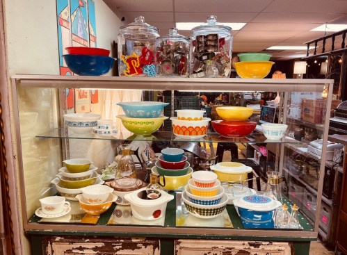 A display case filled with colorful vintage bowls and kitchenware in a shop.