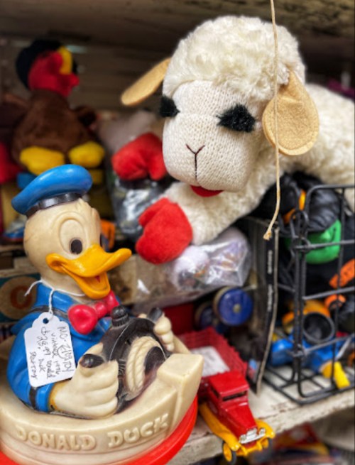 A Donald Duck toy and a plush sheep among various colorful toys and trinkets on a shelf.
