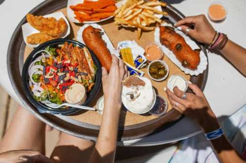 A tray of food featuring corn dogs, fries, sweet potato fries, a salad, and ice cream, with hands reaching for the dishes.