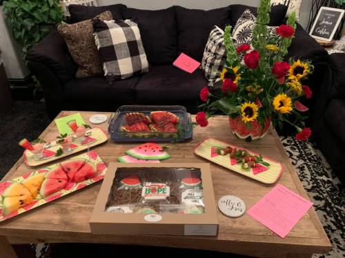 A cozy living room with a coffee table displaying watermelon-themed snacks and a vibrant flower arrangement.