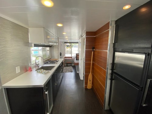 Modern kitchen with sleek black and white cabinetry, stainless steel appliances, and a wooden paddle on the wall.