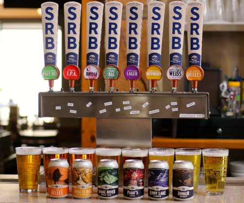 A row of beer taps with various labels above, and a selection of beer cans and glasses in front on a bar counter.