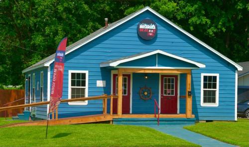 A blue house with a wooden ramp, featuring a sign for a seafood restaurant and a "Now Open" banner.