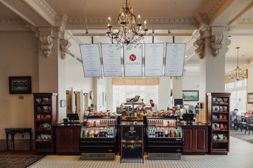 A cozy café interior featuring a counter with pastries, drinks, and a menu hanging above in an elegant setting.