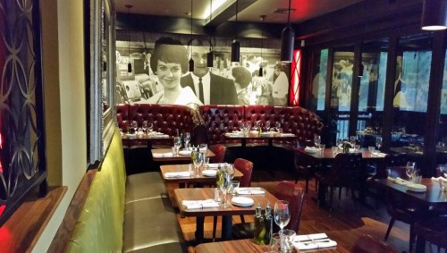 A stylish restaurant interior with red booths, wooden tables, and a large black-and-white mural on the wall.