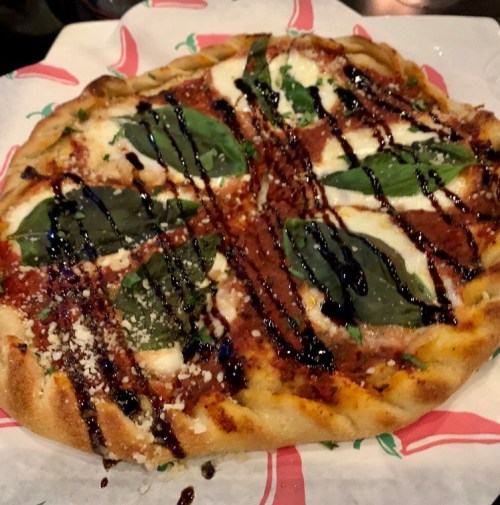 A freshly baked pizza topped with mozzarella, basil, and drizzled with balsamic glaze on a decorative plate.