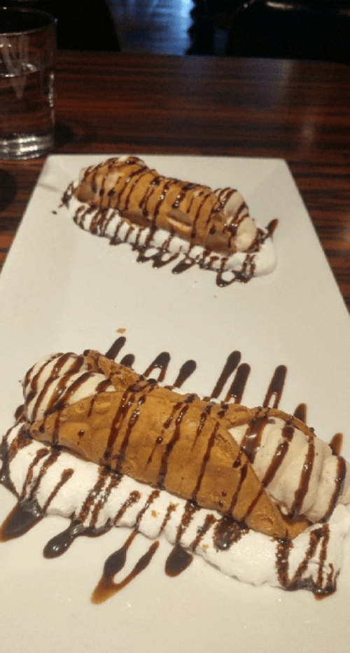 Two dessert cannoli drizzled with chocolate sauce, served on a white plate with whipped cream.