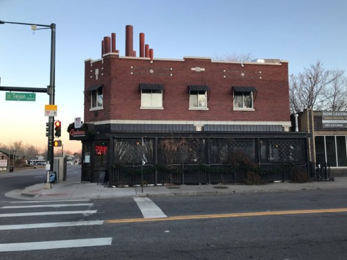 A brick building with multiple windows and chimney stacks, located at a street corner with traffic lights.