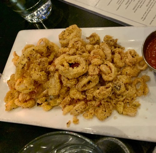 A plate of crispy fried calamari served with a side of marinara sauce.