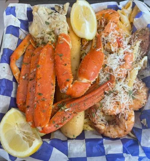 A seafood platter featuring crab legs, shrimp, potatoes, and lemon wedges on a blue and white checkered paper.