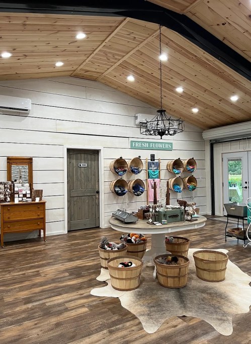 A cozy shop interior with wooden beams, baskets of flowers, and a display of fresh flowers on the wall.
