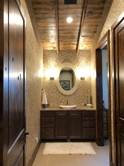 A stylish bathroom with a wooden ceiling, patterned walls, a round mirror, and a modern sink and vanity.