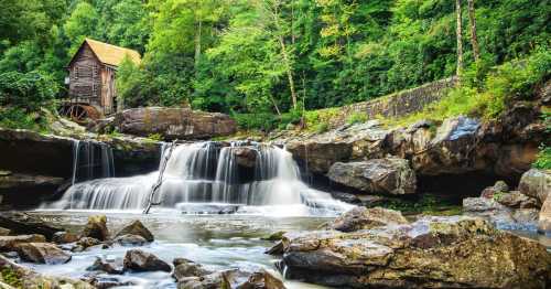 A serene scene of a wooden mill by a waterfall, surrounded by lush green trees and rocky terrain.