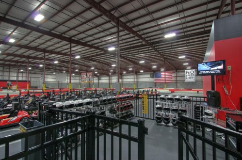 Indoor go-kart racing facility with karts lined up, safety barriers, and an American flag displayed overhead.