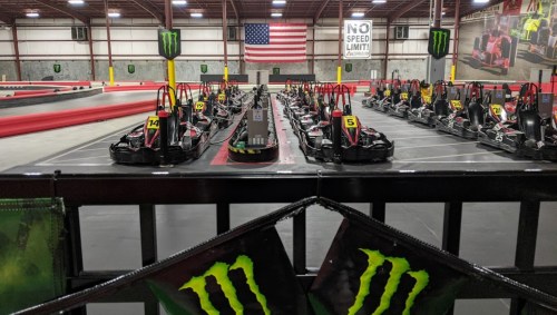 A go-kart track with multiple karts lined up, an American flag in the background, and a "No Speed Limit" sign.