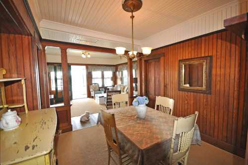 A cozy dining area with a wooden table, chairs, and a vase of flowers, featuring warm wood paneling and natural light.