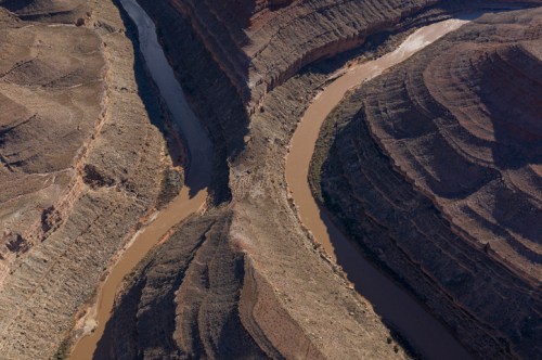 Aerial view of a winding river cutting through rugged, layered canyon terrain.
