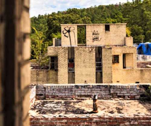 Abandoned building with graffiti, surrounded by trees and a clear blue sky in the background.