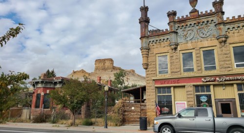 Historic buildings with unique architecture in a small town, set against a backdrop of a rocky hill under a cloudy sky.