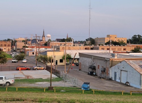 A view of a small town with buildings, a water tower, and parked cars under a clear sky.