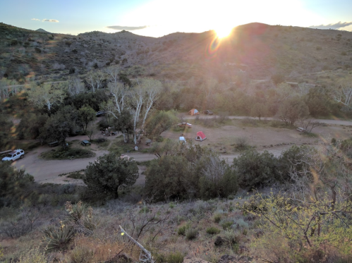 A scenic view of a campsite in a valley, with tents and trees, illuminated by a setting sun in the background.