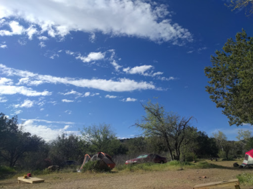 A scenic campsite with tents, trees, and a clear blue sky dotted with clouds.