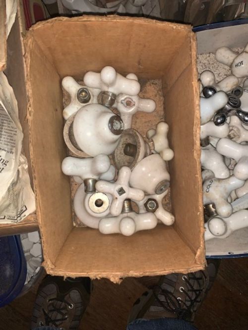 A cardboard box filled with various white ceramic knobs and hardware pieces, resting on a wooden surface.