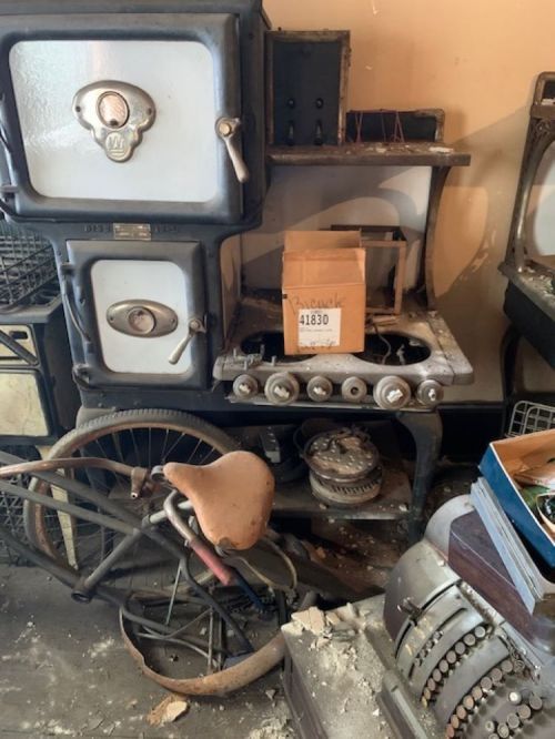 An old, rusty stove and various vintage items cluttered in a dusty room.