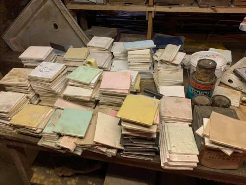 A cluttered workspace filled with stacks of colorful tiles and a can of paint, creating a vibrant, artistic atmosphere.