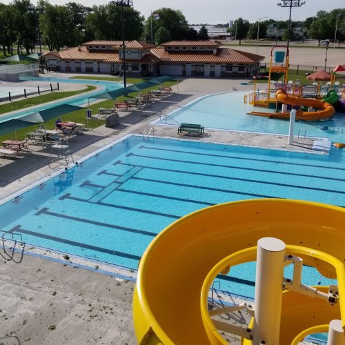 Aerial view of a water park featuring empty swimming pools and a yellow water slide on a sunny day.