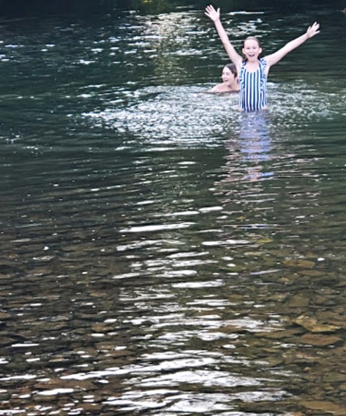 Two children play in a shallow, clear water area, splashing and enjoying a sunny day.