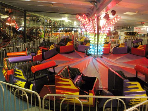 A colorful amusement ride with seats arranged in a circular pattern, surrounded by barriers and bright lights.