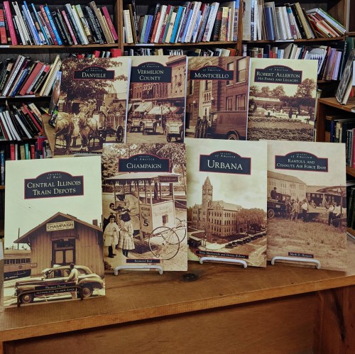 A display of historical books about Central Illinois towns, featuring images and titles on stands in a library setting.