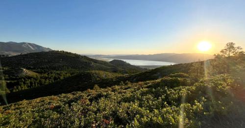 A scenic view of rolling hills and a lake at sunset, with the sun casting a warm glow over the landscape.