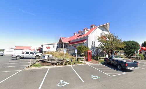 A white building with a red roof, surrounded by parking spaces and trees, under a clear blue sky.