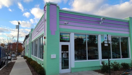 A colorful building with purple and green stripes, featuring large windows and an "Open" sign.