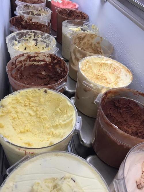 A row of various ice cream flavors in clear containers, including chocolate, vanilla, and strawberry.