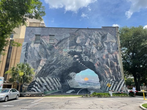 A large mural depicting a tunnel with a sunset and road, set against a blue sky and trees.